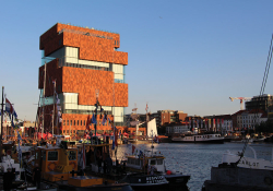 A blocky, multi-story building rises out of a river in Antwerp