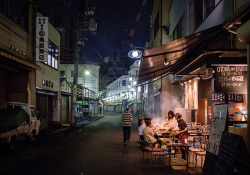 A group of people sit at a table in front of a street vendor in Nagoya, Japan