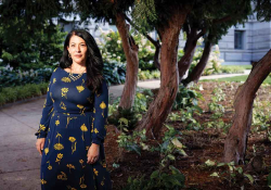 A photograph of Ada Límon who stands in front of a small tree garden