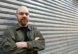 A photograph of Ariel Magnus, who stands with his arms crossed, in front of a lowered eaves