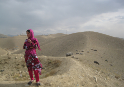 A woman stands on a ridge of sand in a desert landscape