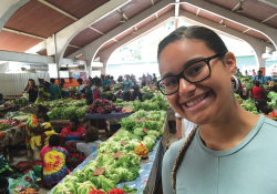 A photograph of a woman smiling at the camera with an open air market in the background