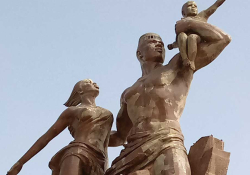 A photograph of a statue of a male figure, holding a baby toward the sun on his shoulder with a woman on his other arm