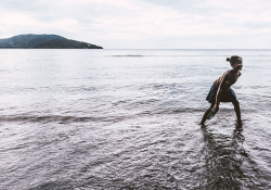 A girl plays in the water on the beach with another island visible in the distance